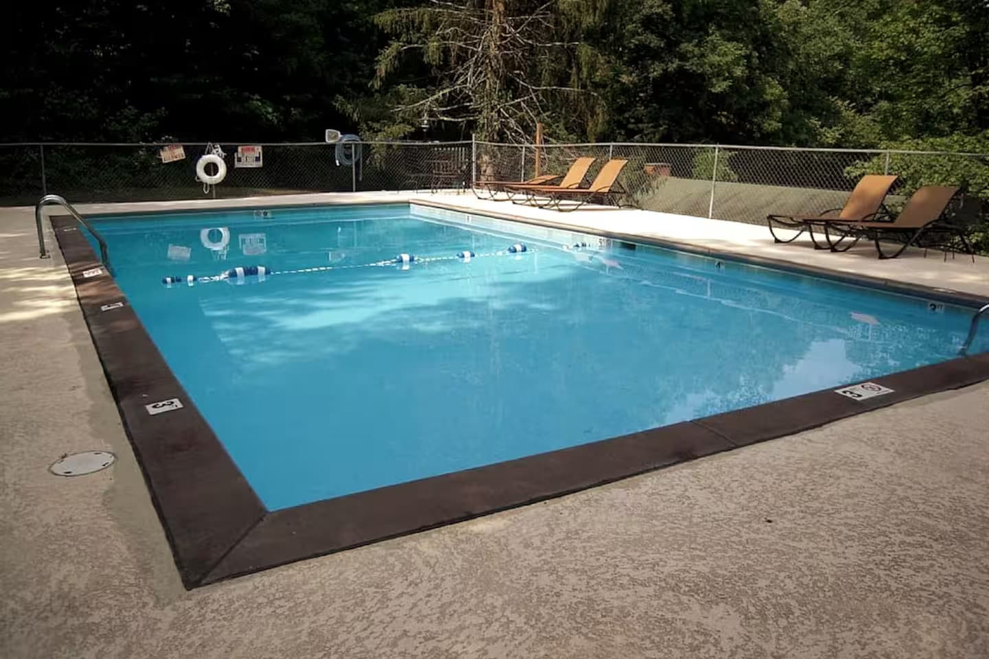 An empty fenced community swimming pool with poolside lounge chairs.