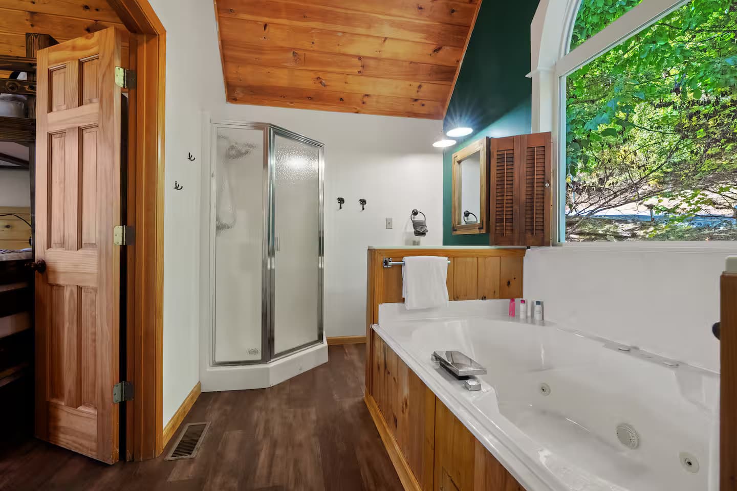 A bathroom with a corner shower stall, a teal accent wall, and an arched shuttered window.