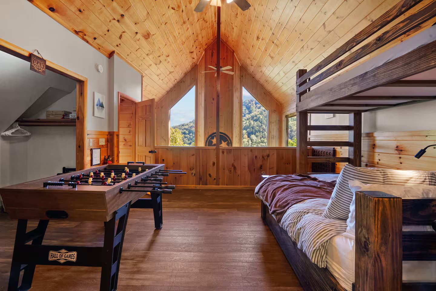 A loft area with a foosball table, a striped daybed, and a gable window with a mountain view.