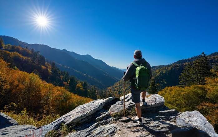 A hiker overlooking an autumn mountain valley beneath a bright blue sky.