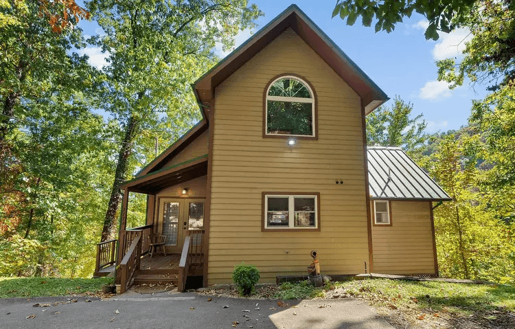 The cabin entrance and front exterior viewed from the driveway beneath mature trees.