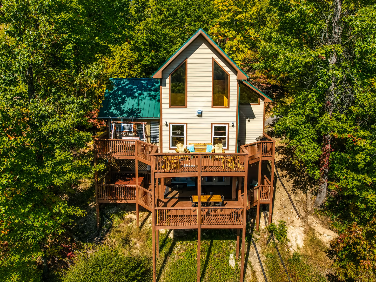 Aerial view of the three-story cabin and its tiered wooden decks surrounded by dense green forest.