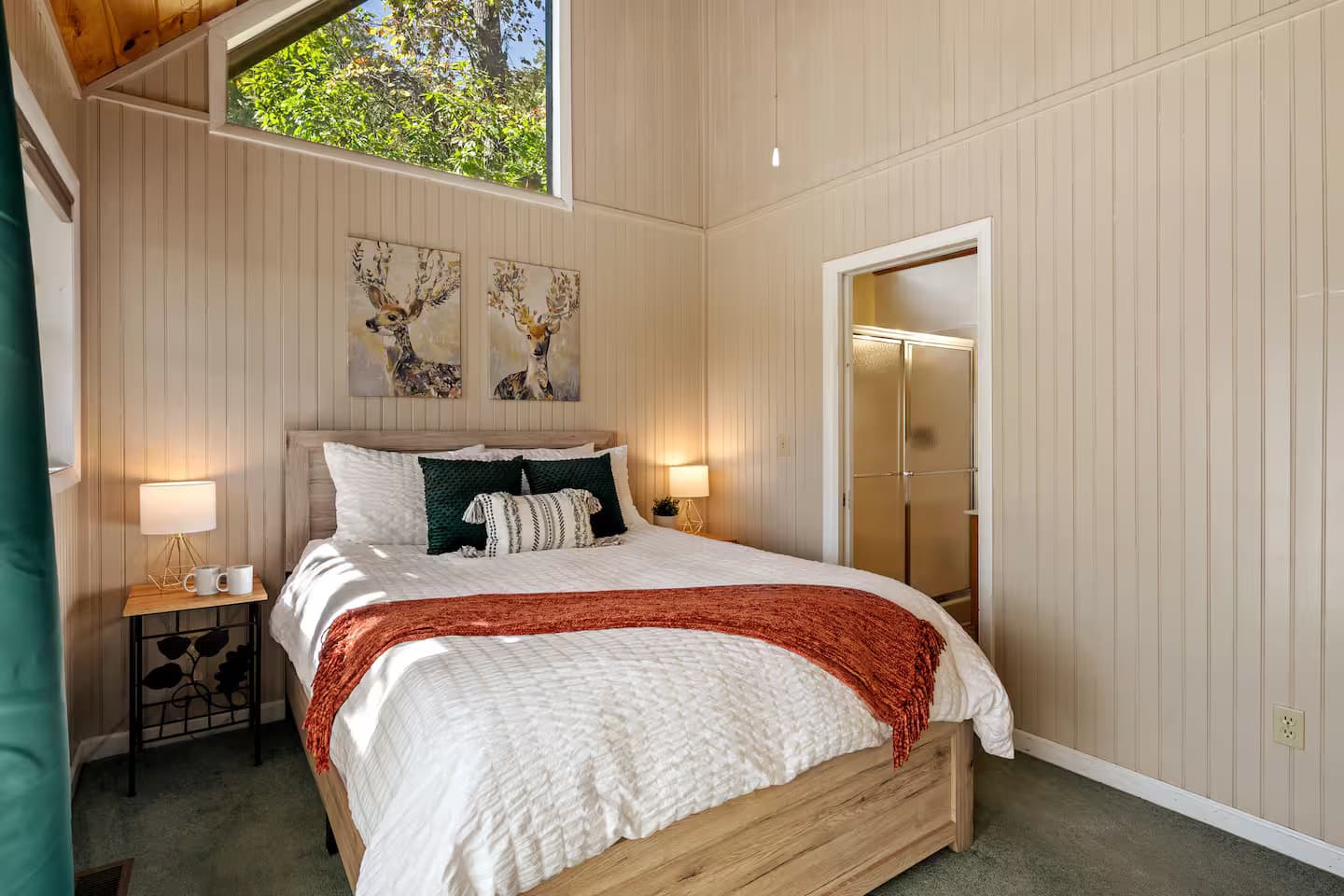 The bedroom's vaulted wood ceiling, peaked treetop window, and glass sliding shower door in the ensuite bathroom.