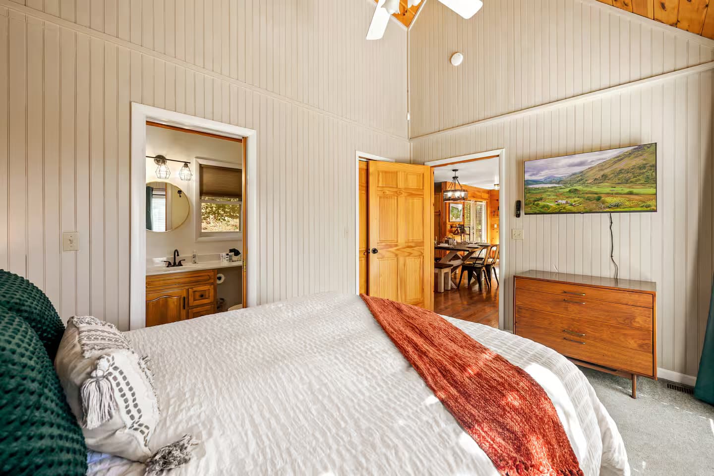 The bedroom viewed wider, showing an open door to an ensuite bathroom and a wall-mounted TV.