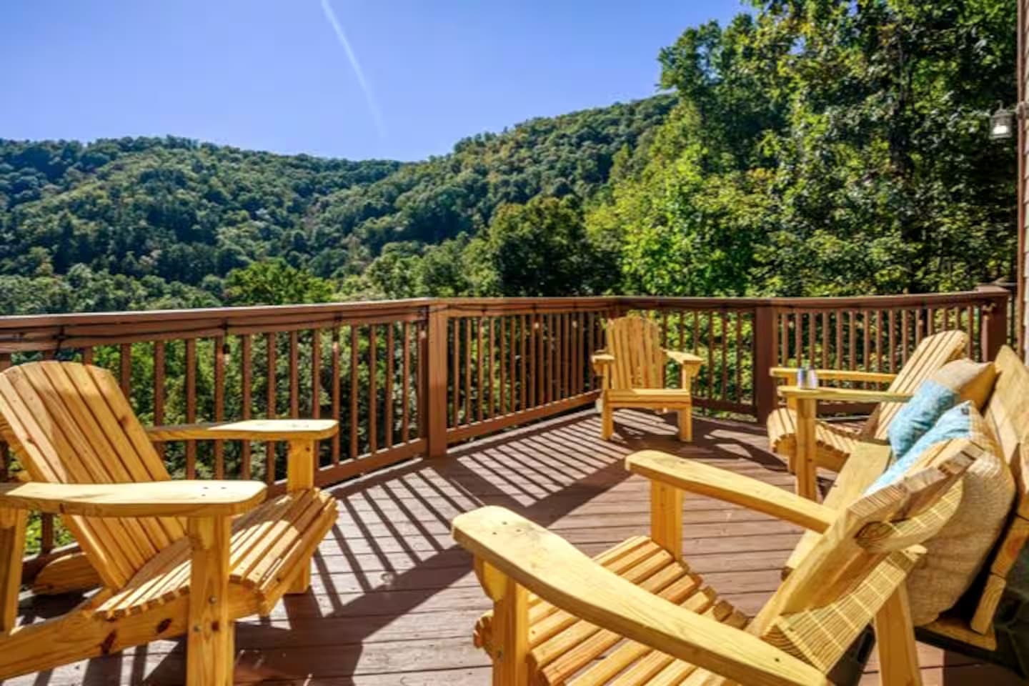 Wooden Adirondack chairs and a cushioned bench on the deck, overlooking green mountain ridges.
