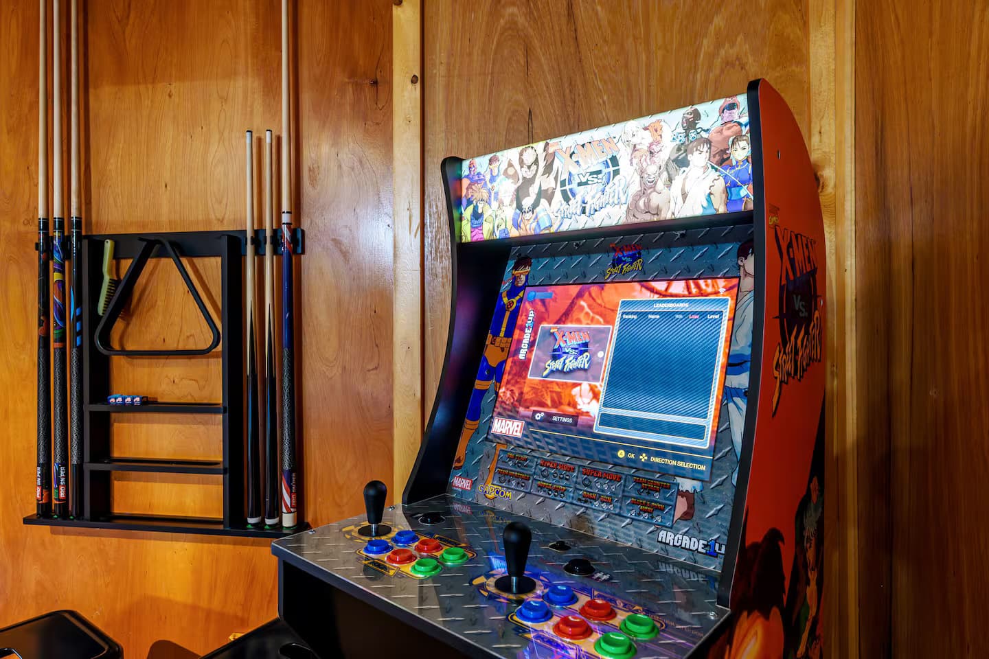 A standing arcade cabinet next to a wall-mounted pool cue rack.