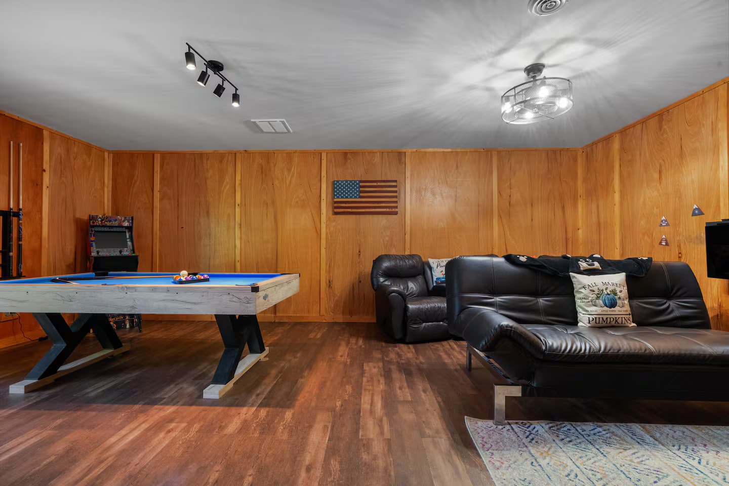 A basement-style rec room with a pool table, an arcade cabinet, and a leather sofa and recliner.