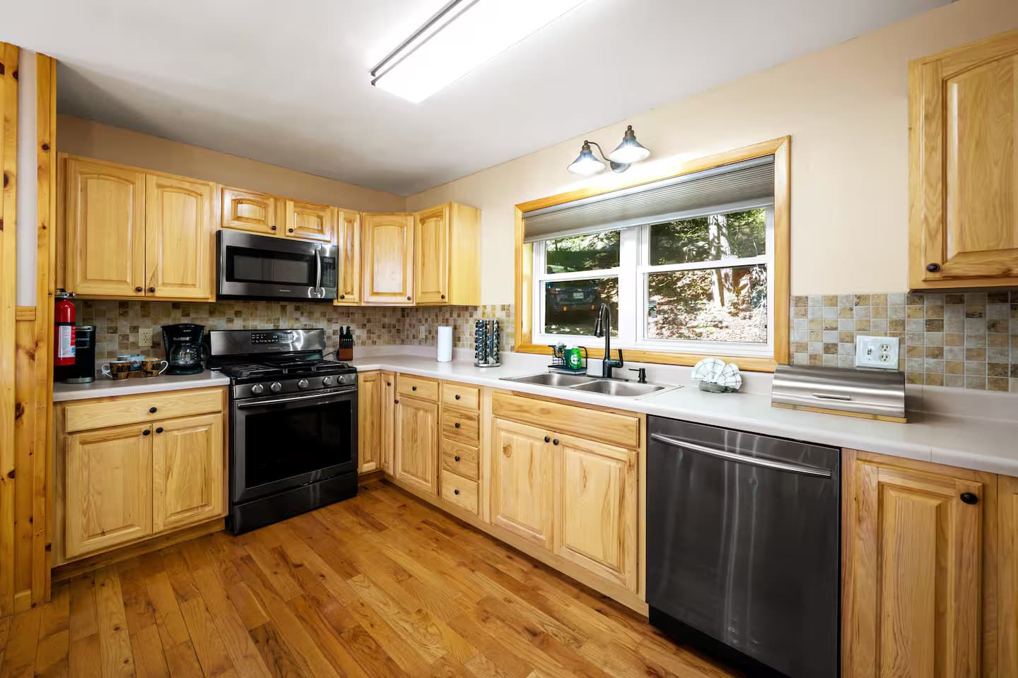An L-shaped wood-cabinet kitchen with a gas range and a window over the sink looking out to the forest.