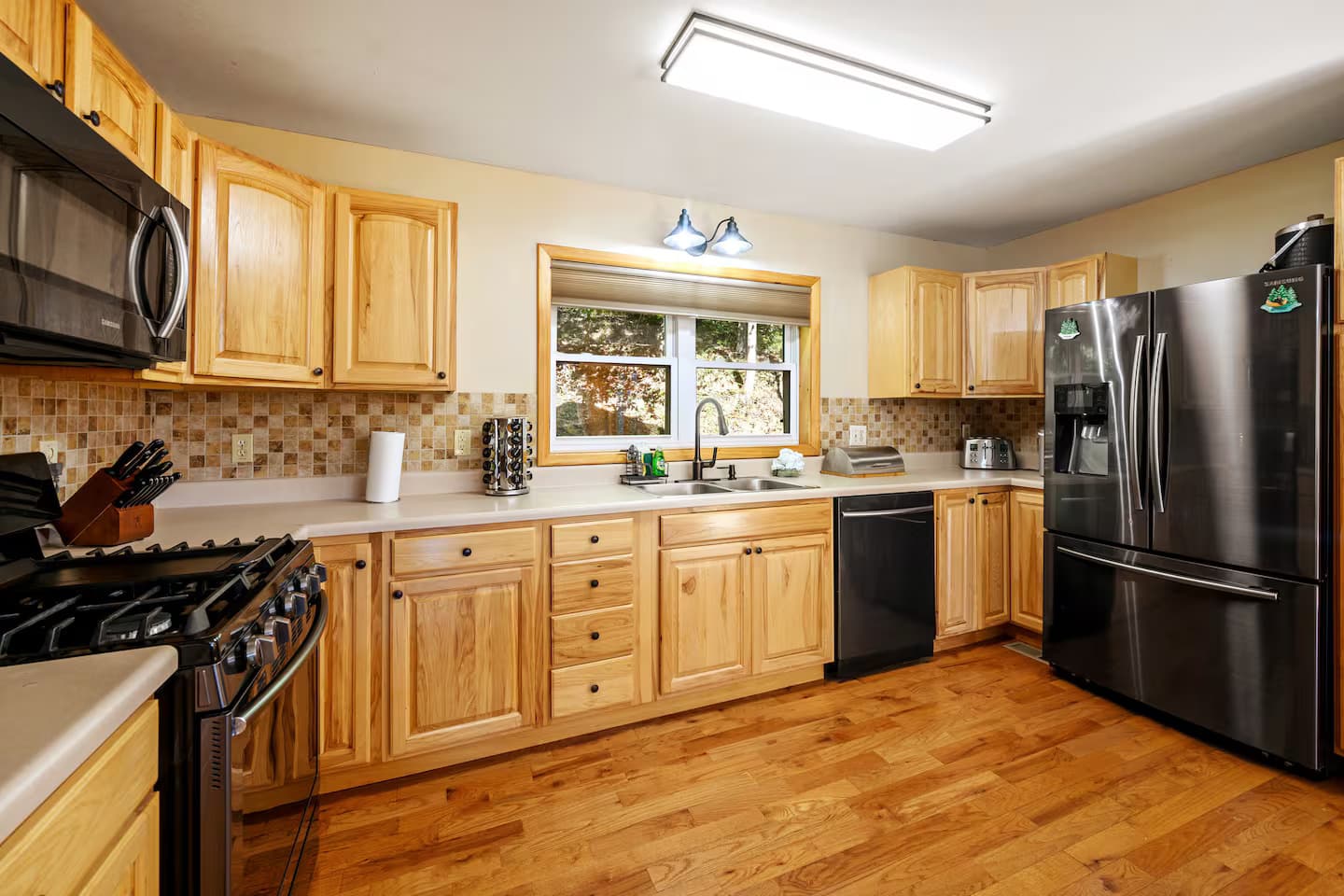 A wood-cabinet kitchen with a black stainless refrigerator, gas range, and dishwasher.