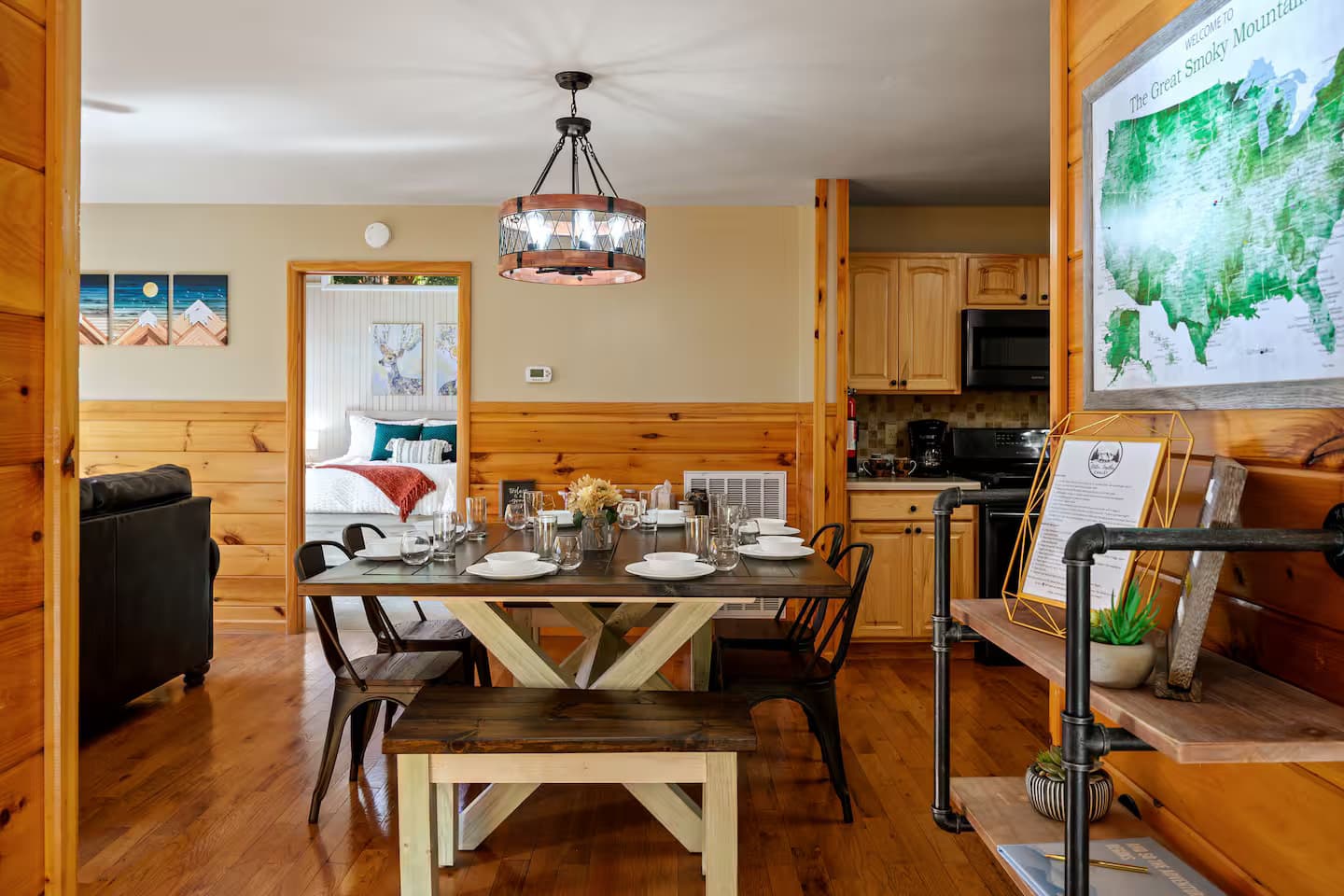 A farmhouse dining table set for six beneath a pendant light, with the kitchen visible beyond.