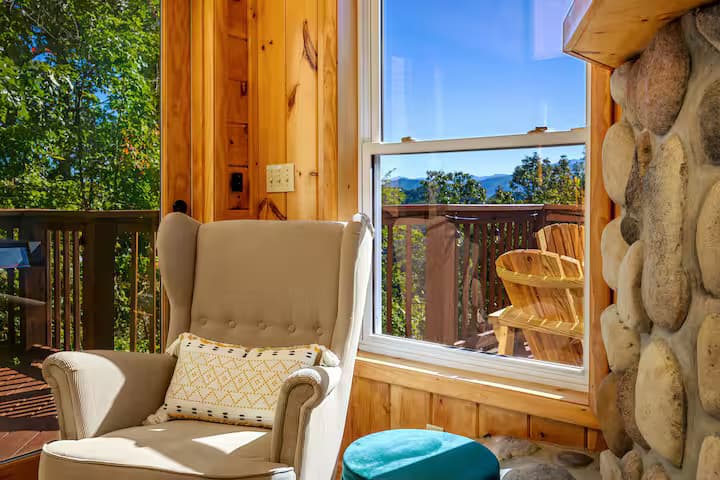 A wingback armchair beside a large window looking out to the deck and a mountain view.