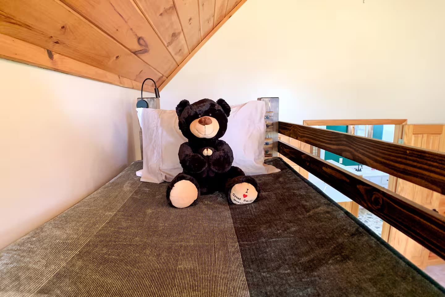 A close-up of the top bunk mattress with a bear-themed pillow, looking down over the rail.