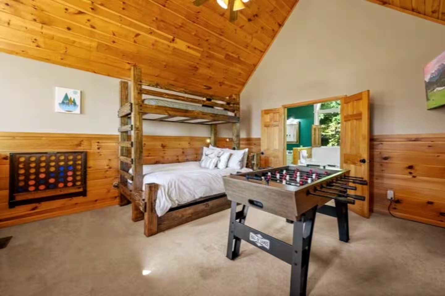 Bunk beds in the loft with a foosball table nearby and a doorway open to an ensuite bathroom.