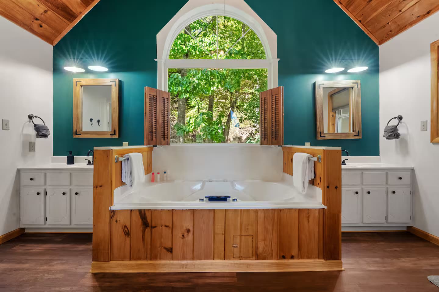 A bathroom with a double vanity, a jetted tub, and an arched window, serving the loft area.