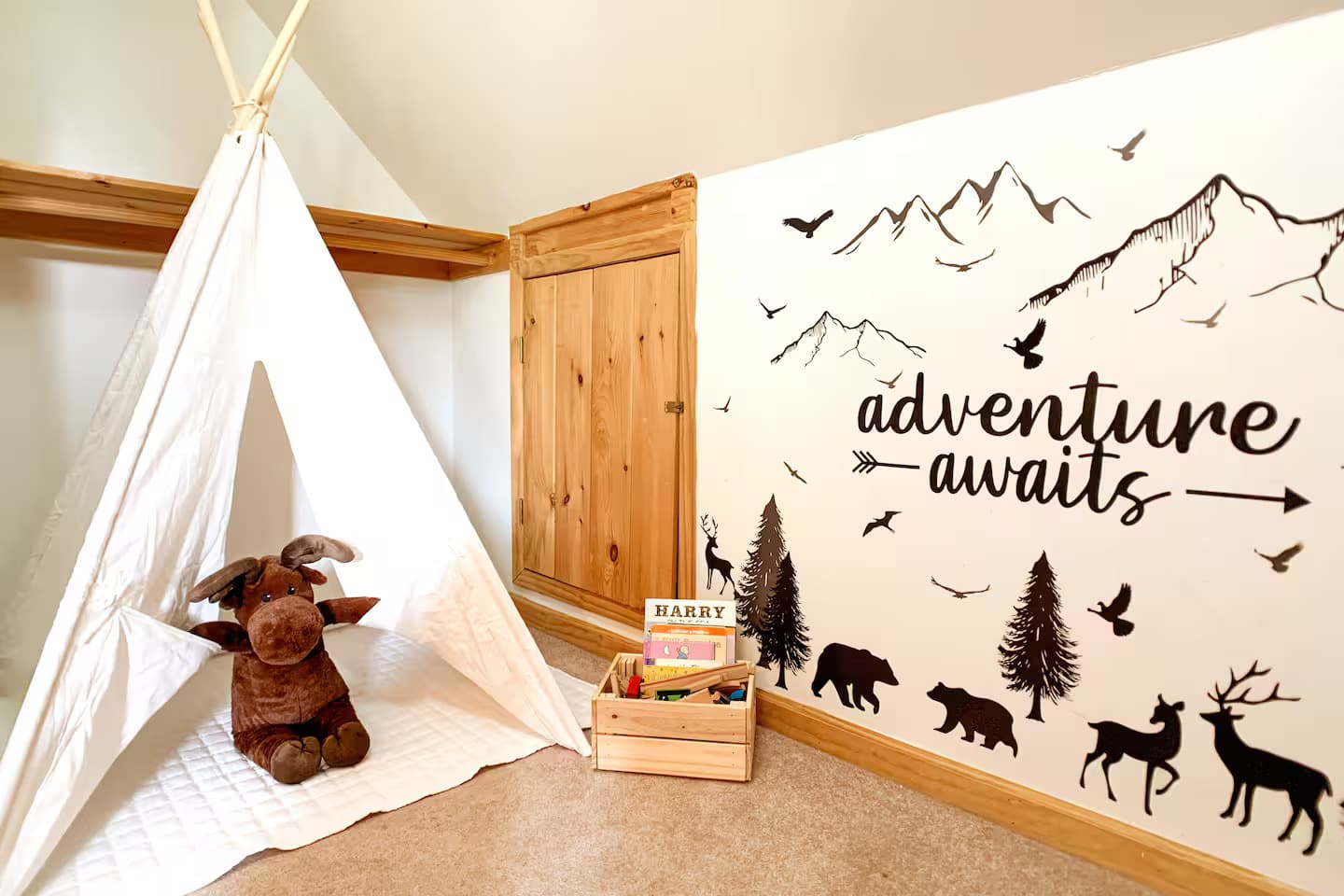 A play teepee, a stuffed moose toy, and a crate of children's books in a corner of the loft.