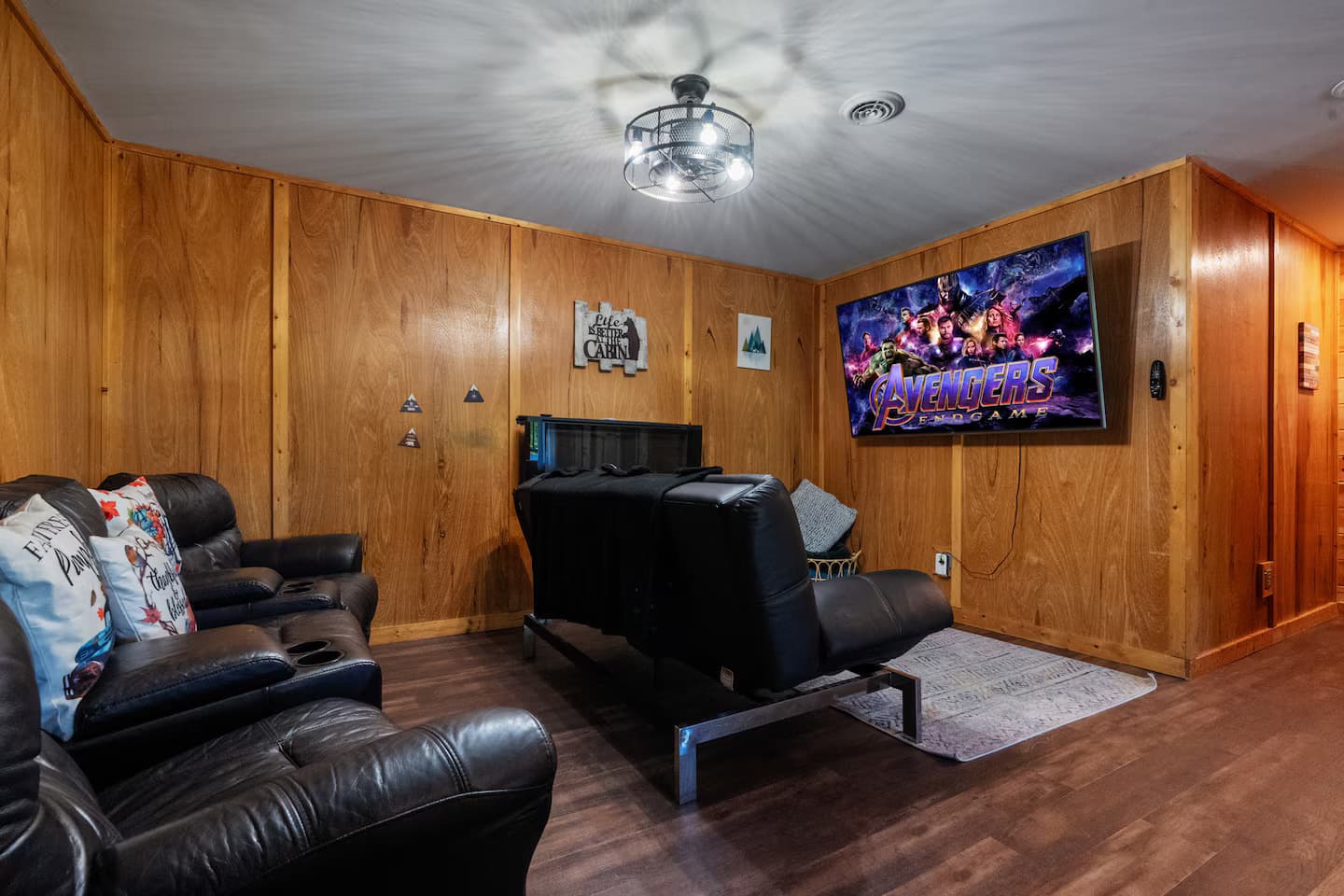 Black leather reclining chairs facing a large wall-mounted TV in a wood-paneled room.