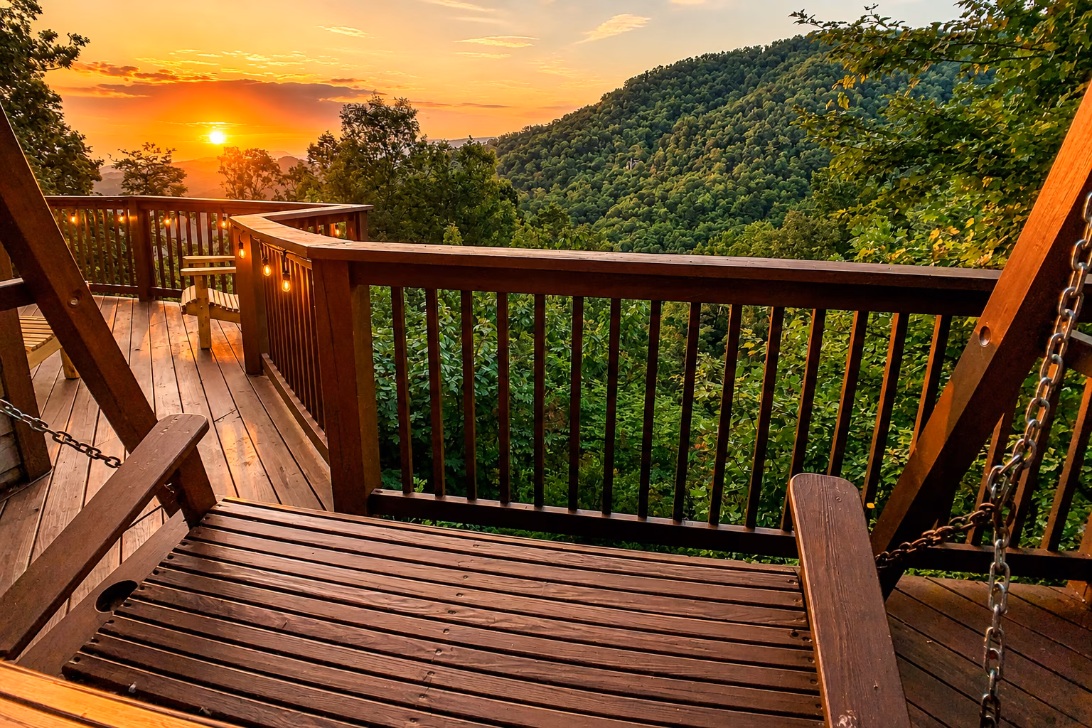 Sunset over layered mountain ridges viewed from a wooden deck swing with string lights along the railing.